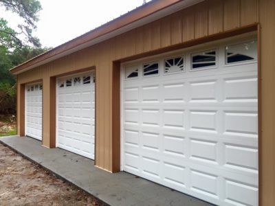 A row of three white garage doors on the side of a house.