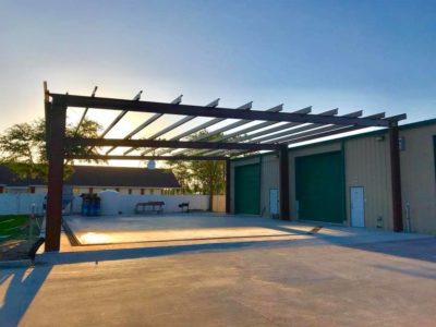A large open garage with a pergola over it.
